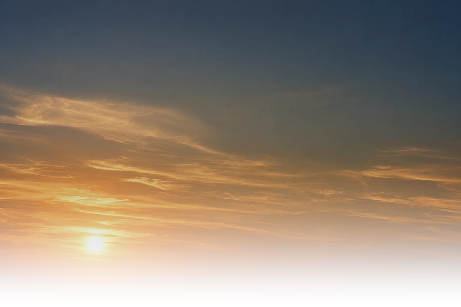 A site engineer standing on a desert rock outcrop at sunset, looking out towards a multi-storey building under construction with a tower crane above it.